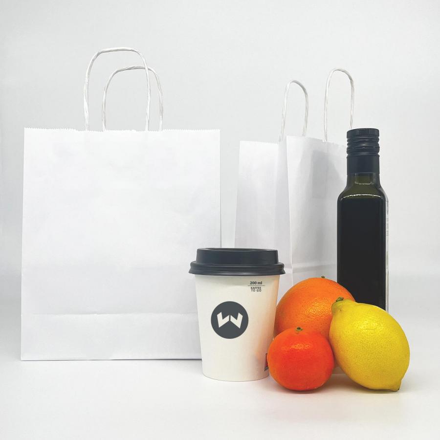Kleine weiße Papiertüte neben Kaffeetasse und Früchten zur Größenveranschaulichung